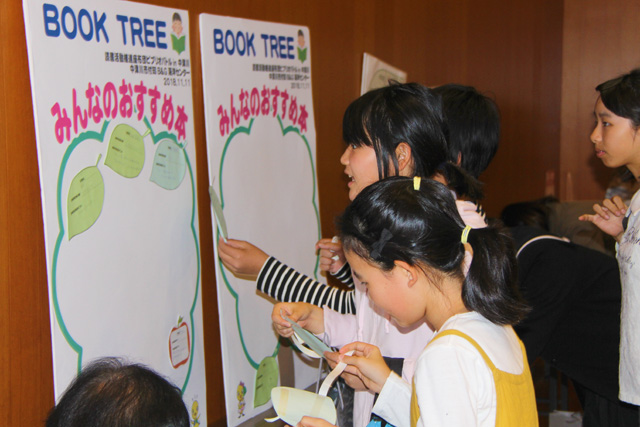 壁に立てかけてある、ブックツリーの樹の絵に、おすすめ本を書いた用紙を貼り付けていく子供たち