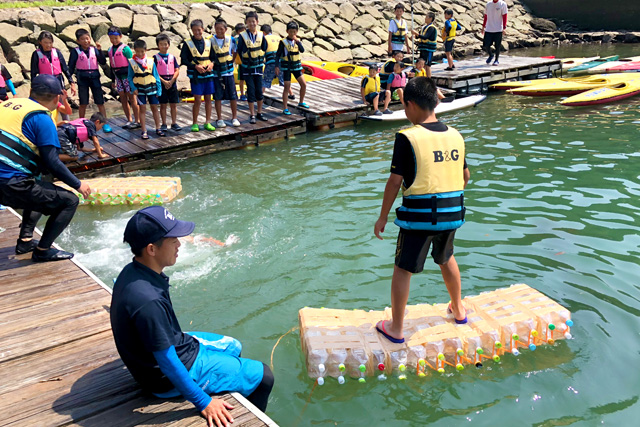 出来上がったペットボトルいかだを海に浮かべて乗ってみる子供