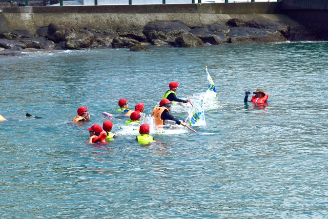 ライフジャケットを着て、海の中で乗ろうとする子供たち