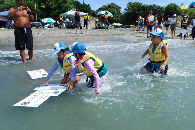 浜辺近くの海面に浮かぶ、大きなカルタのカードを、水の中を移動しながら探す子供たち