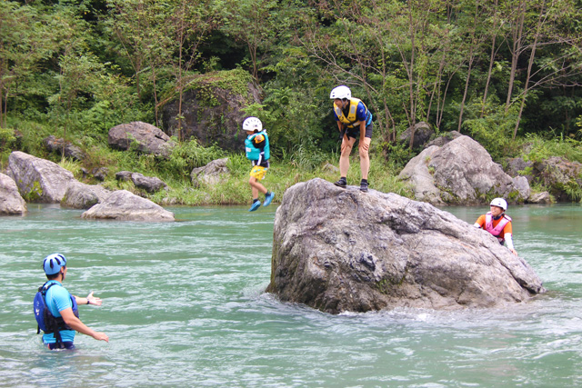 川の中にある、大きな岩の上から川に向かって飛び込む子供