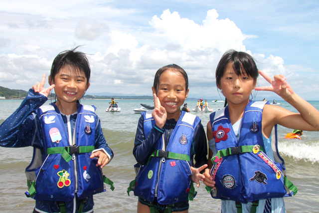 オリジナルライフジャケットを着て、浜辺で笑顔でピースサインする女の子たち
