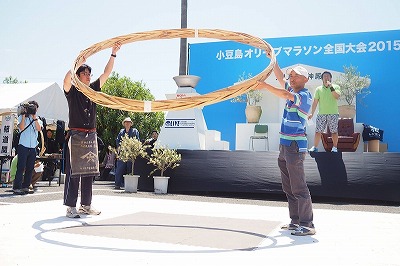 タガの重さは13kg。左が大会を発案した山本康夫さんです。 昨年の優勝者は、この大きな輪を225回も回しました。はたして今年は・・・ 