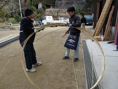 タガを編む山本さん（右）と大工の坂口町会議員。 山本さんは、この大きな輪をフラフープにすることを思いつきました 