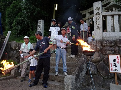 神社の入り口で、子供たちの火手に火をつけています。火手は、一度火をつけたら20～30分は燃え続けるように松脂や布を使って工夫しています