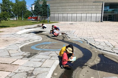 屋外にある、模型を見ながら学習中の親子の画像