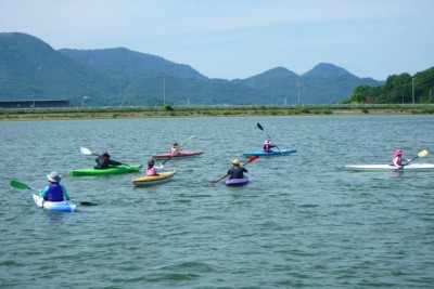 1人用のカヌーに乗った6人の人々が川面に浮かぶ