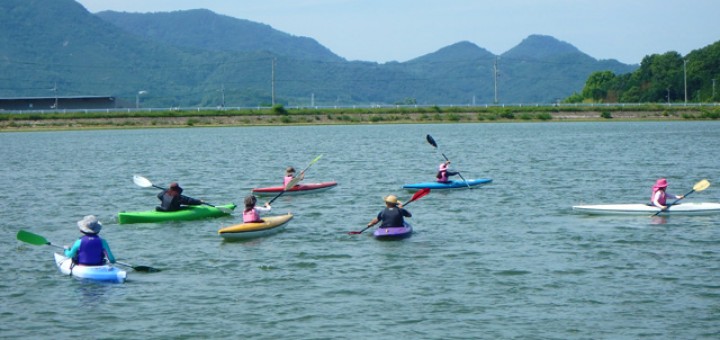 1人用のカヌーに乗った6人の人々が川面に浮かぶ