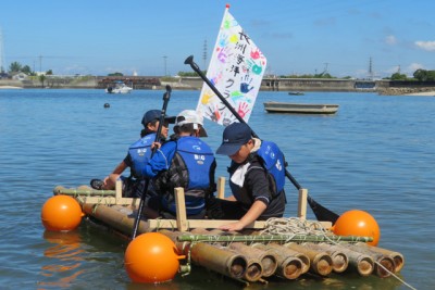 竹のイカダに乗って海に漕ぎ出す3人の男の子たち