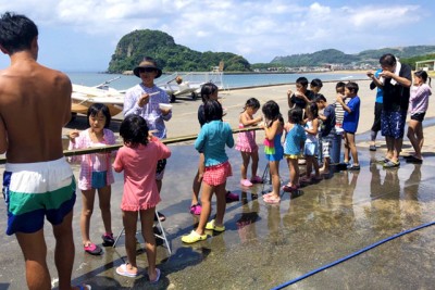 流しそうめんが流れてくる、ながい竹の周りで、流れてくるそうめんを待ち受ける子供たち