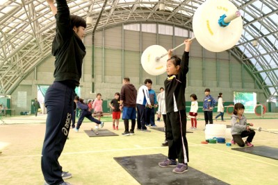 大きな模擬の巨大なダンベルを頭上に持ち上げる女の子