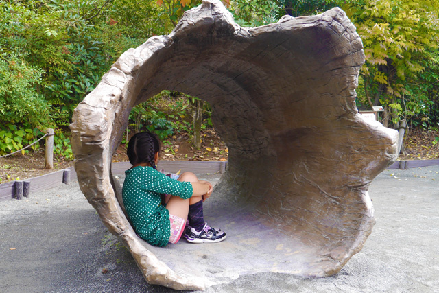 中が空洞の土管に似た遊具の中で膝を抱える女の子の画像
